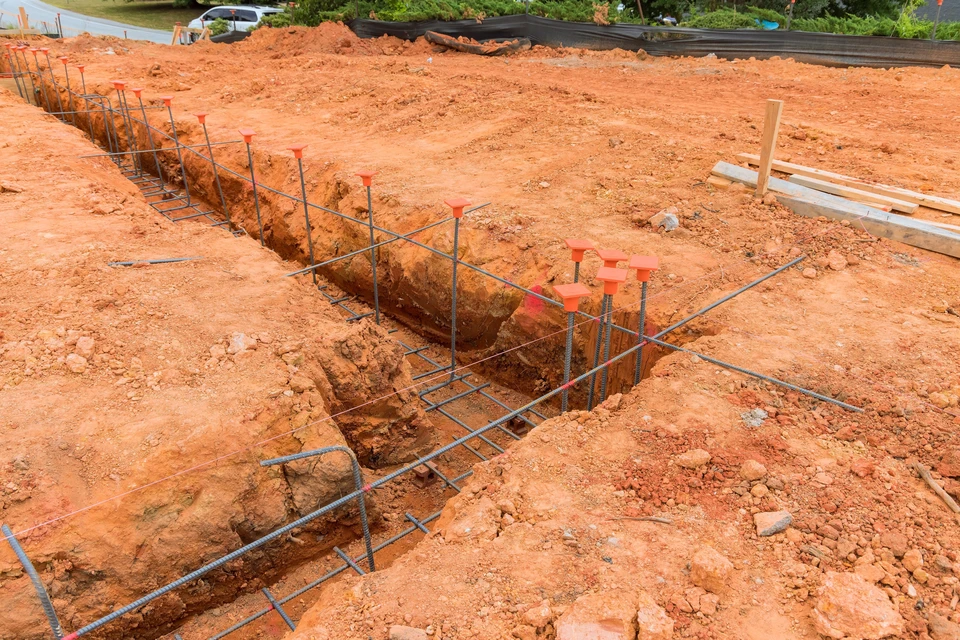 Chantier de construction extérieur avec tranchées excavées dans sol argileux rouge
