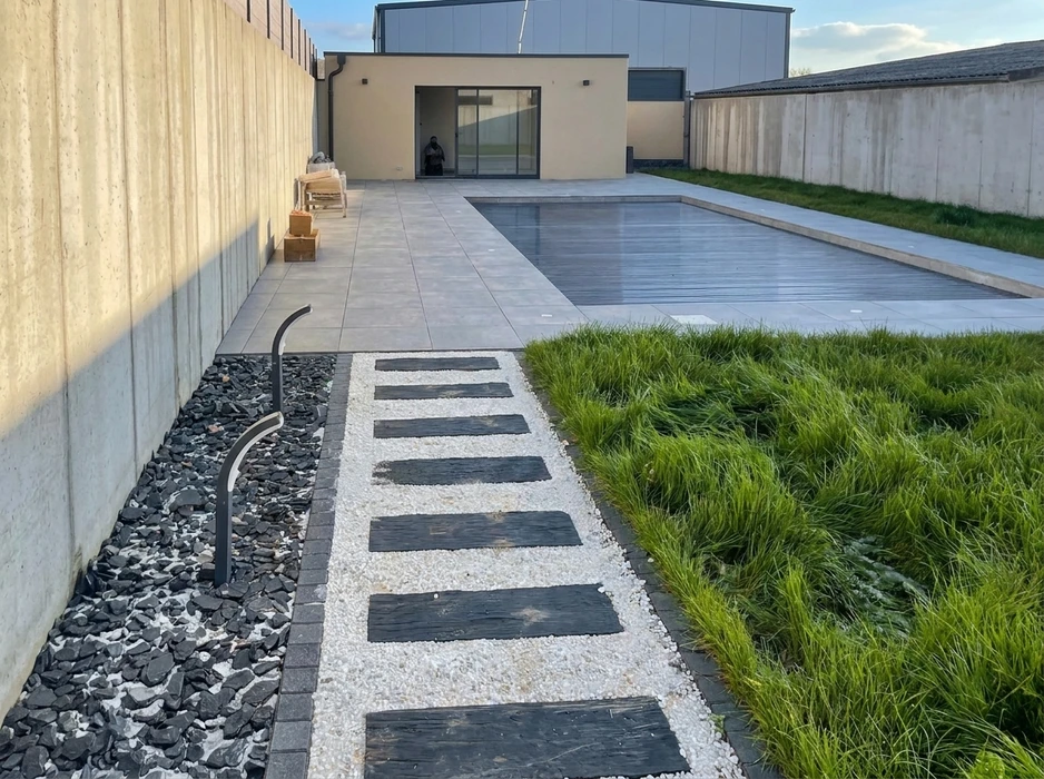 Jardin contemporain extérieur, allée piétonne avec dalles en ardoise noire posées sur graviers blancs, bordée de graminées ornementales