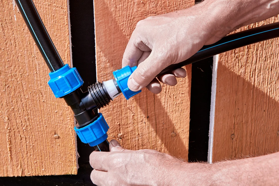 Scène extérieure, mains d'un technicien assemblant des raccords de plomberie contre une clôture en bois