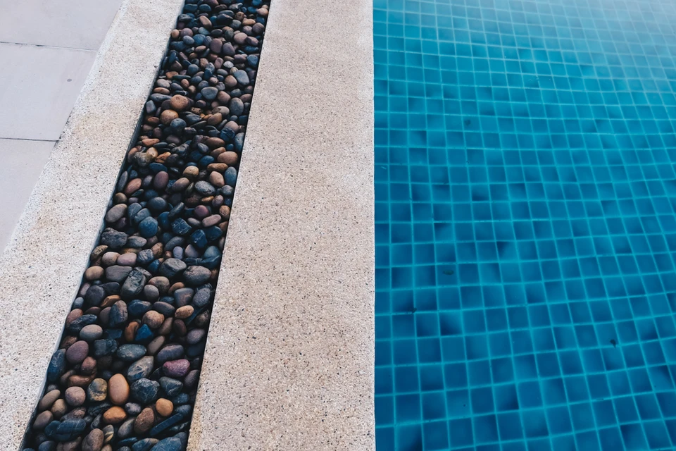 Extérieur piscine avec margelle en béton désactivé, bordure décorative en galets de rivière multicolores et revêtement carrelage bleu turquoise