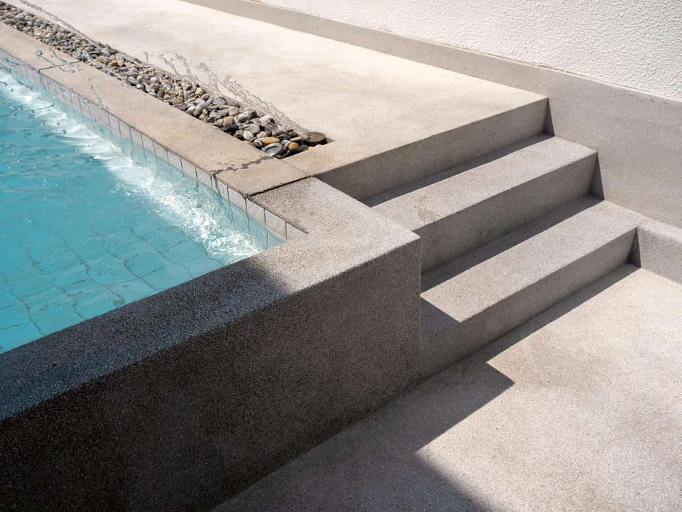 Am&eacute;nagement ext&eacute;rieur de piscine avec margelles en b&eacute;ton gris dispos&eacute;es autour du bassin carrel&eacute; de mosa&iuml;ques turquoise